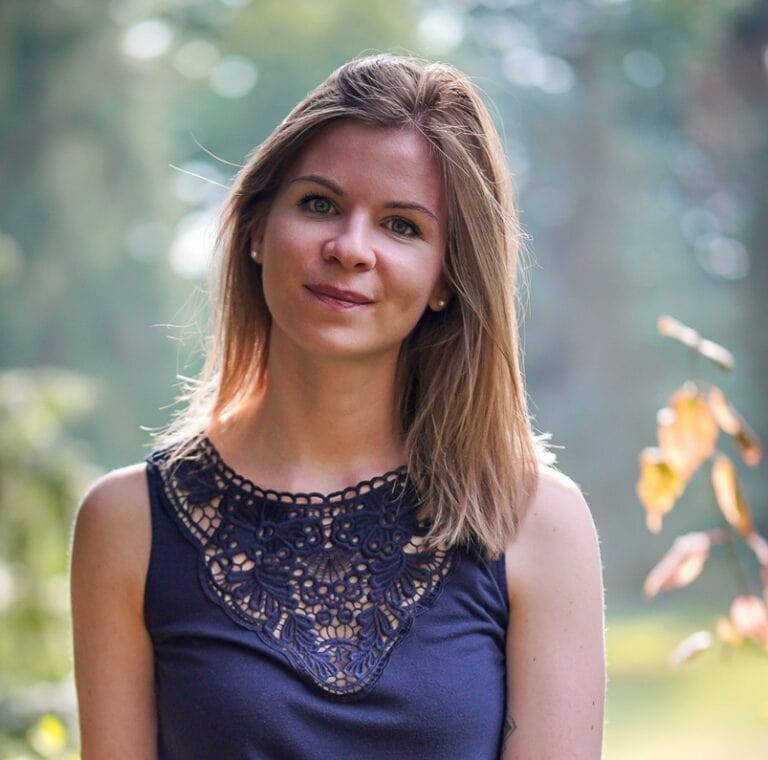 Lydia Hannes sitzt im Vordergrund einer hellen Waldlichtung.