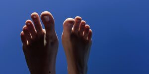 Zwei nackte Füße vor einem kräftig blauen Hintergrund, von warmem Licht sanft beleuchtet – ein ruhiges, minimalistisches Bild für Selbstliebe, Selbstannahme und Körperliebe sowie für ein gesundes Selbstwertgefühl und die Wertschätzung der eigenen inneren Werte.