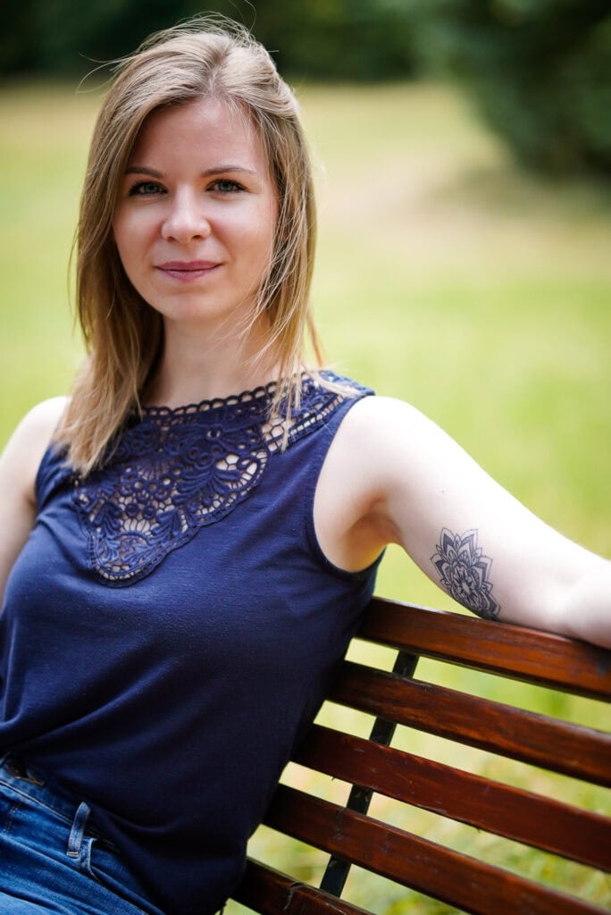 Lydia Hannes, Coachin für hochsensible Frauen, sitzt entspannt auf einer Bank im Park und schaut freundlich in die Kamera.